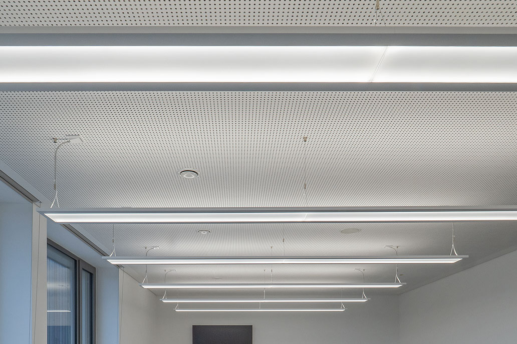 Gelochte Akustikdecke mit Pendelleuchten im Klassenraum